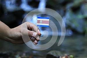 National flag of Costa Rica on wooden stick with water background. Colour man holds state symbol and waves. Concept of humanity