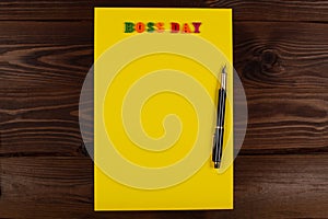 National Happy Boss Day. Multicolored colorful letters in a yellow blank page with pen on the table. Bosses day office photo