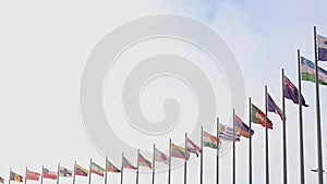 National state flags of many countries waving in the wind on the alley of flagpoles against the background of blue sky