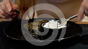 National traditional cuisine food in the restaurant. Woman is eating dolma with sour cream served in clay plate, dish closeup