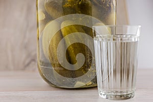 National trait harmful to health: a large jar of pickles and faceted glass of Russian vodka on a white table, front view