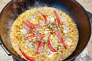 National Uzbek dish pilaf, pilaw, plov, rice with meat in big pan. Cooking process in a cauldron on fire. Preparation