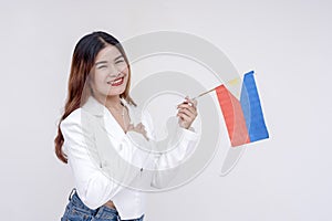 A nationalistic young woman holding one hand to her chest and holding a Philippine flag while smiling at the camera. Isolated on a photo