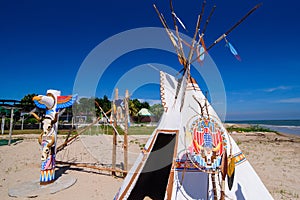 Native american indian tepee and totem pole on the beach blue sk