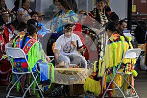 Native Americans dressed in intricate and colorful traditional outfits sing a song and drum at a powwow in San Francisco