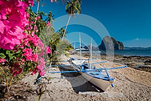 Native banca boat and vibrant flowers at Las cabanas beach with amazing Pinagbuyutan island in background. Exotic nature