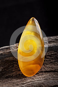 Natural amber. A piece of yellow opaque natural amber on large piece of dark stoned wood.