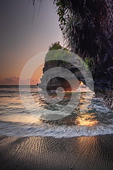 Natural arch. Batu Bolong temple on the rock during sunset. Seascape background. Motion milky waves on black sand beach. Copy