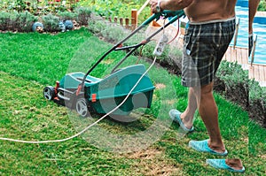 Natural background A man mows a lawn mower with a green lawn in his own garden near a flower garden in summer. Side view,