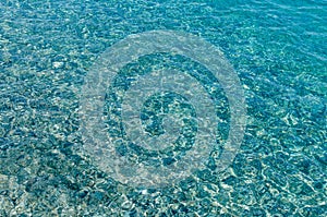 Natural background of transparent azure sea water and bottom with rocks. A close-up view of the pebbles on the beach