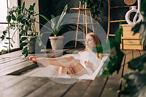 Natural beautiful blonde young woman taking bath with bubbles in bathroom interior with plenty green plans