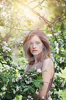 Natural beauty. Beautiful female model girl with brown hair in spring blossom park. Young perfect woman on spring flowers