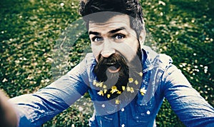 Natural beauty concept. Hipster on happy face sits on grass, defocused. Man with beard enjoys spring, green meadow
