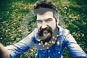 Natural beauty concept. Hipster on happy face taking selfie photo. Man with beard enjoys spring, green meadow background