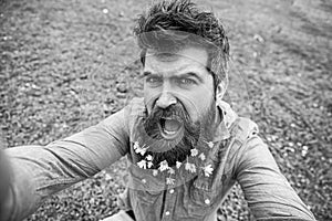 Natural beauty concept. Man with beard enjoys spring, green meadow background. Hipster on shouting face sits on grass