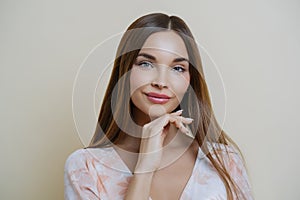 Natural beauty and people concept. Portrait of beautiful dark haired young European woman touches jawline gently, dressed in