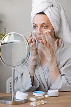 natural beauty and skin care, beautiful young caucasian woman applies cream on her face, beauty of face and body, skin