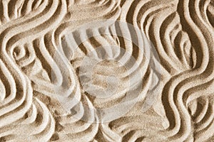 Natural beige sand texture background with wave pattern. Wavy curved ornaments on sand, drawn by hand. Top view