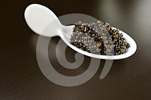 Natural black caviar in a white porcelain spoon on a dark background. Product segment. Place for the inscription