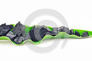 Natural black wood cosmetic activated charcoal or mineral with medicinal properties on green leaf isolated on white background