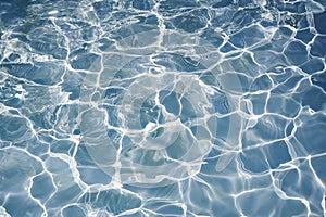 Natural blue water surface with bright sun light reflections. blue water in swimming pool background