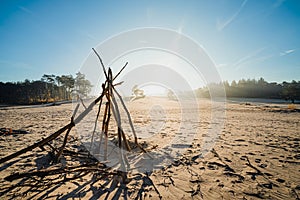 Natural children\'s hut built with sticks on sand with rising morning sun