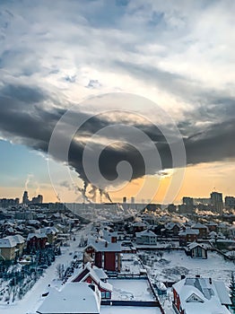 Natural city background. Aerial view of the city winter landscape at sunset  roofs of small houses in the snow and thick clouds