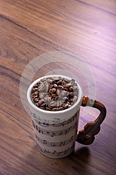 Natural coffee beans in an artistic musical cup. Music notes painted on the cup with a cello shaped handle. International Coffee