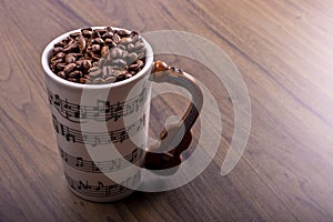 Natural coffee beans in an artistic musical cup. Music notes painted on the cup with a cello shaped handle. International Coffee