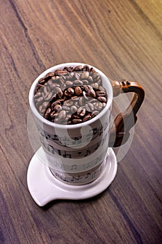 Natural coffee beans in an artistic musical cup. Music notes painted on the cup with a cello shaped handle and a white plate.