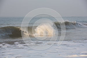 Natural copy space shot of a wave crushing on the smooth yellow sand beach surface, forming white foam, with the blue sky on the