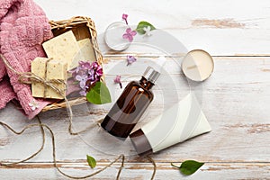 Natural cosmetics with lilac flowers. Serum, soap and cream with towel rolls.
