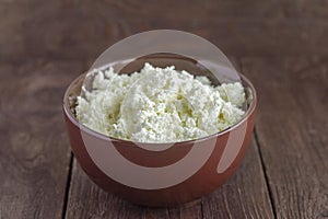 Natural cottage cheese in a bowl on a dark wooden table, close-up view. Calcium-rich healthy food