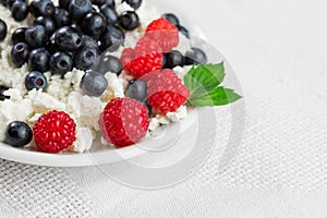 Natural cottage cheese with raspberries and blueberries on a white plate, with mint leaves