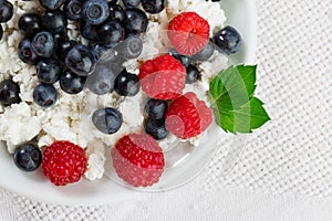 Natural cottage cheese with raspberries and blueberries on a white plate, with mint leaves