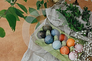 Natural dye easter eggs in carton tray on rustic table with flowers. Modern yellow, pink, blue and grey easter eggs painted with