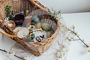 Natural dyed easter eggs, easter bread, ham, beets, butter, cheese in wicker basket decorated with green buxus on rustic wooden