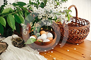 Natural Easter eggs, wicker basket, bird nest and cherry flowers on rustic table. Happy Easter, atmospheric moment. Rural still