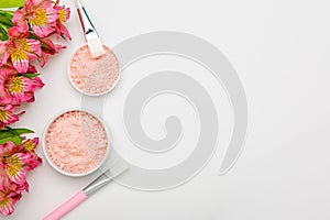 Natural facial mask in jars and with brushes on white background with flowers. Pink alginate clay mask with kaolin and