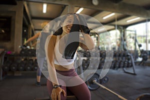 Natural fitness club lifestyle portrait of young happy and attractive Asian woman training at gym bench wiping the sweat with