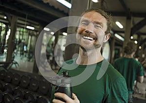 Natural fitness lifestyle portrait of young happy and attractive man drinking bottle of water training at gym smiling cheerful