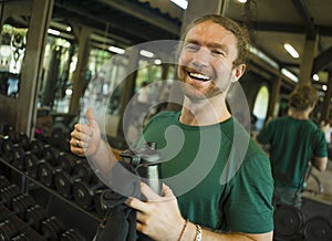 Natural fitness lifestyle portrait of young happy and attractive man holding bottle of water training at gym smiling cheerful