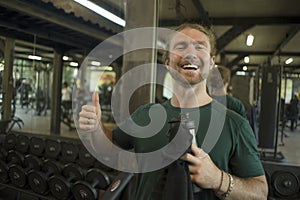 Natural fitness lifestyle portrait of young happy and attractive man holding bottle of water training at gym smiling cheerful