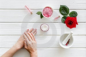 Natural floral cosmetics with rose flowers for face and body care and female hands on white wooden background top view