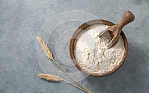 Natural flour in a wooden bowl with a scoop on a blue background with branches of dry wheat. Organic and healthy product for home