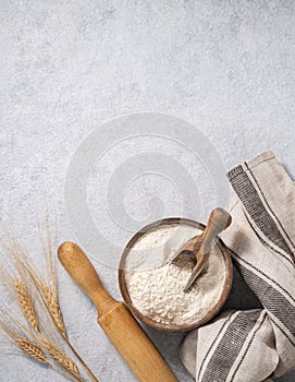 Natural flour in a wooden bowl with a scoop, rolling pin and napkin on a blue background with branches of dry wheat. Organic and