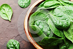 Natural fresh baby spinach leaves in wooden bowl on vintage stone table. Organic healthy food.