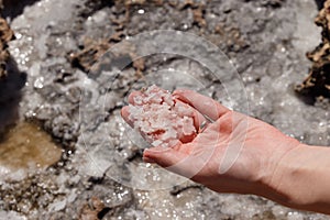 Natural frozen sea salt in the girl`s hand. Backgrounds and texture on the seashore in stone deposits flooded with water and the
