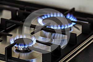 Natural gas burning on kitchen gas stove in the dark. Panel from steel with a gas ring burner on a black background, close-up shoo