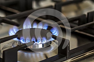 Natural gas burning on kitchen gas stove in the dark. Panel from steel with a gas ring burner on a black background, close-up shoo